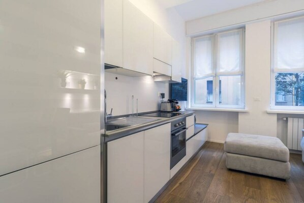 A modern kitchen with white cabinets, stainless steel appliances, and a window providing natural light.