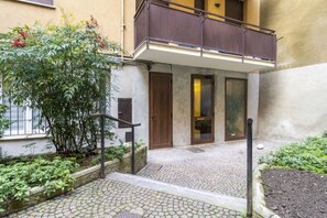 A courtyard with cobblestone paths, a wooden door, and a balcony with a metal railing.