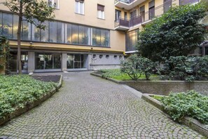 A courtyard with cobblestone paths, a building with large windows, and greenery.