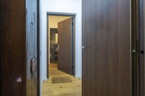 A hallway with wooden flooring and a door leading to a room with a visible shower area.