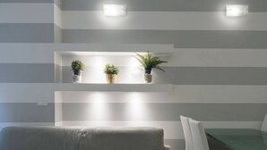 Una sala moderna con un sofá gris, una mesa de comedor de vidrio y tres estantes con plantas.
