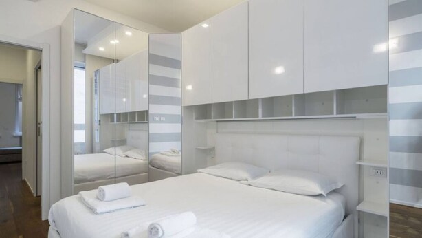 Una habitación de hotel moderna con una cama grande, un armario con espejo y una estantería empotrada.