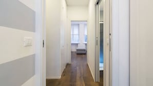 Un pasillo estrecho con suelo de madera y paredes blancas que conduce a una habitación con ventana y un banco.
