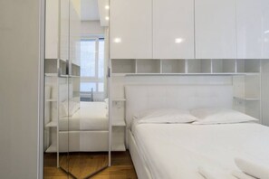 A modern bedroom with a bed, white wardrobe, and a glass partition.