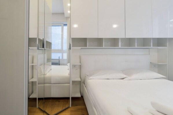A modern bedroom with a bed, white wardrobe, and a glass partition.