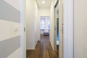 Un pasillo estrecho con suelo de madera y paredes blancas que conduce a una habitación con ventana y un banco.