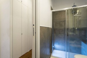 A modern bathroom with a glass-enclosed shower, a toilet, and a white wardrobe.