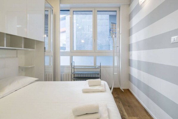A hotel room with a bed, a window, a radiator, and a striped wall.