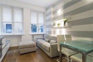 A modern living room with a glass-top dining table, a sofa, and a small ottoman.