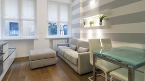 Una sala de estar moderna con una mesa de comedor de vidrio, un sofá y un pequeño reposapiés.