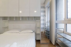 A modern hotel room with a large bed, built-in shelving, and a view through a glass door.