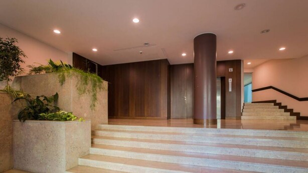 Un hall d’hôtel moderne avec un escalier, une grande colonne et un bac à plantes orné de verdure.