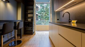 Une cuisine moderne dotée d’un four encastré, d’un évier et d’une fenêtre donnant sur un balcon avec un arbre.