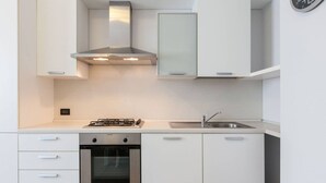 A modern kitchen with white cabinetry, a stainless steel range hood, a gas stove, an oven, and a sink. - Easylife - Spacious and new apt in Città Studi (Milano)