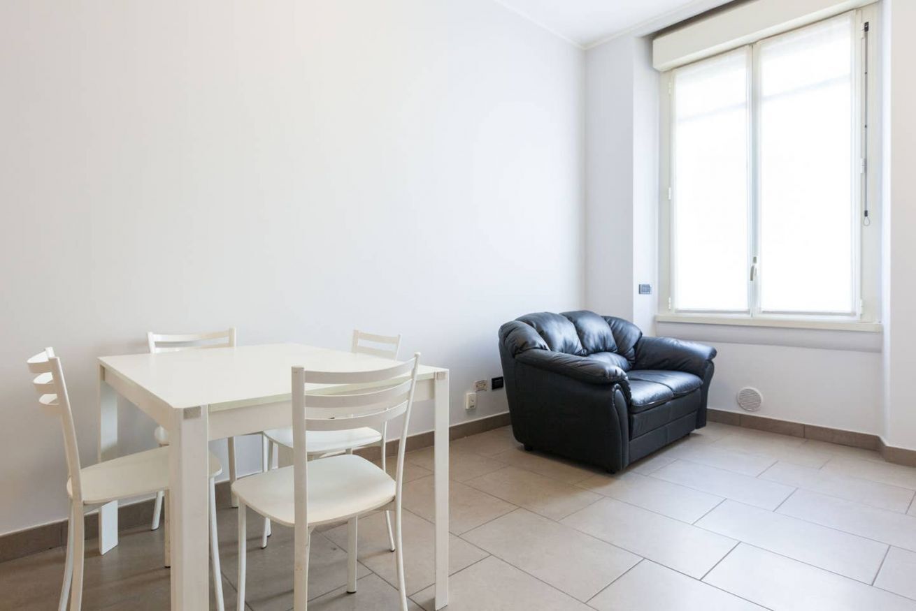 A room with a white table and chairs, a black leather sofa, and a large window.