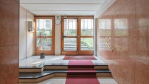 A hotel lobby with a red carpeted staircase leading to a double door entrance.