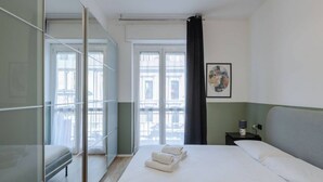 A hotel room with a bed, a nightstand, a window with curtains, and a view of the outside.