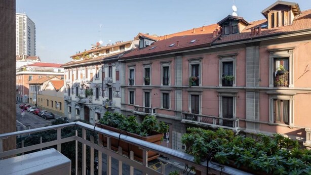 A row of pink buildings with balconies, a street in the background, and a clear sky.