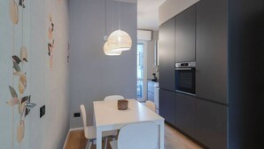 A modern kitchen with dark cabinets, a white dining table, and a hanging pendant light.