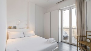 A modern hotel room with a large bed, a wardrobe, a seating area with a chair, and a view through a glass door. - Easylife - Comfort in Pta Romana with terrace (Milano)