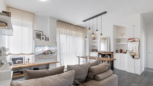 A modern living room with a sofa, a TV, and a dining area with a table and chairs. - Easylife - Comfort in Pta Romana with terrace (Milano)