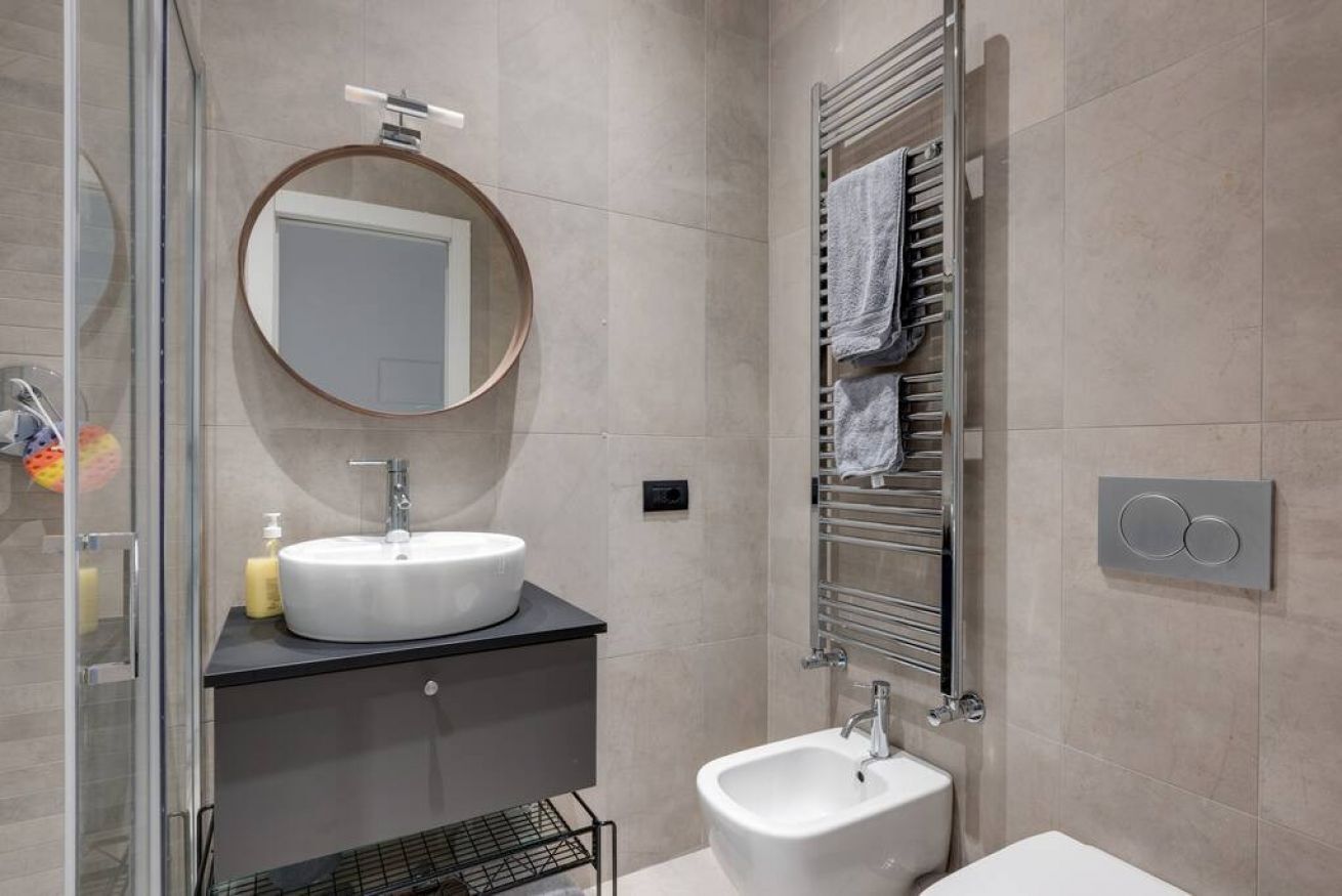 Un baño moderno con un espejo redondo, un lavabo, un bidé y un perchero para toallas.