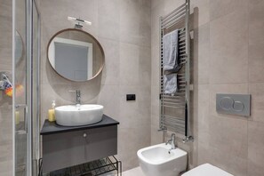 Une salle de bain moderne avec un miroir rond, un lavabo, un bidet et un porte-serviettes.