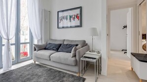 A modern living room with a grey sofa, a small side table, and a framed artwork on the wall.
