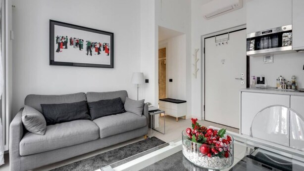 A modern living room with a grey sofa, a framed artwork, a small side table, and a glass coffee table with a decorative arrangement.