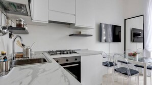 A modern kitchen with a marble countertop, stainless steel appliances, and a glass dining table with chairs.