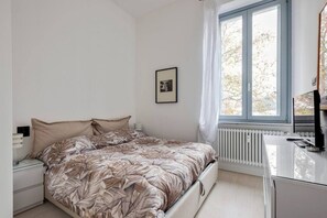 Une chambre à coucher avec un lit, une table de chevet, une fenêtre avec des rideaux et un radiateur.