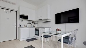 A modern kitchen with white cabinets, a built-in oven, and a glass dining table with chairs.