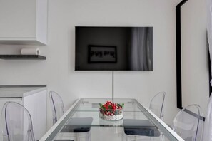 Un espace repas moderne avec une table en verre, des chaises transparentes, une œuvre d’art encadrée au-dessus, et un petit bol décoratif posé sur la table.