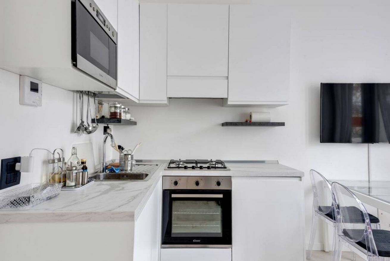 Una cocina moderna con armarios blancos, horno empotrado, cocina a gas y televisor de pantalla plana montado en la pared.