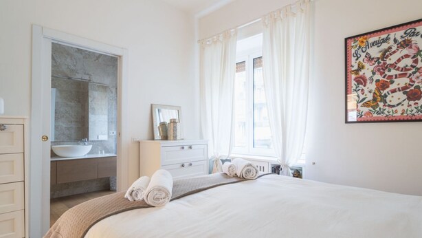 Ein Schlafzimmer mit einem großen Bett, ein Badezimmer mit Waschbecken und Spiegel sowie ein Fenster mit Vorhängen.