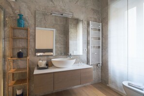 Une salle de bain moderne avec un grand lavabo blanc, un miroir, un porte-serviettes et une étagère en bois.