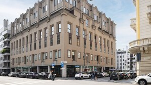 A multi-story building with a symmetrical facade, large windows, and a ground-level entrance with a 'P' parking sign. - Easylife - Precious Pearl in Porta Romana (Milano)