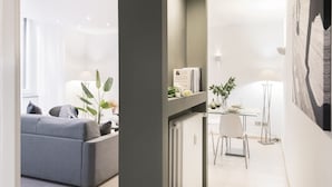 Una sala moderna con un sofá gris, una mesa de comedor con sillas y un radiador. Hay una planta sobre la mesa y una lámpara junto a ella.