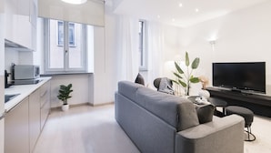 Una sala de estar moderna con un sofá gris, un televisor de pantalla plana y una pequeña mesa de comedor.