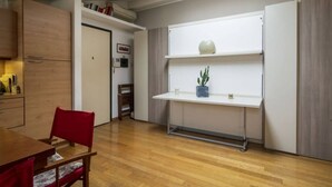 A compact kitchen with wooden cabinets, a white countertop, and a built-in white refrigerator. - Easylife - Cozy studio apartment in Navigli area (Milano)