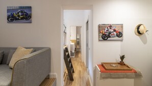 Un salon moderne avec un canapé gris, un plancher en bois et un couloir menant à une chambre.