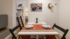 Un coin repas avec une table dressée pour deux personnes, un tableau représentant une moto accroché au mur et un chapeau suspendu au mur.