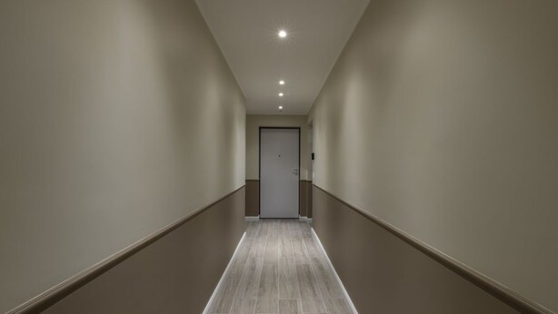 Un couloir étroit et bien éclairé, avec une porte au bout.
