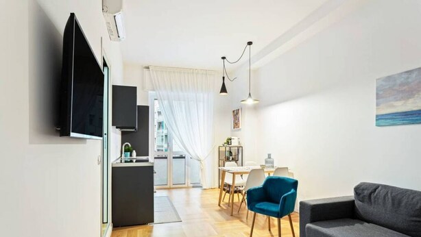 A modern living room with a grey sofa, a blue armchair, and a dining area with a table and chairs. - Easylife - Design and new flat in Navigli district (Milano)