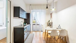 A modern kitchen with a built-in island, a dining area with a table and chairs, and a view through a glass door. - Easylife - Design and new flat in Navigli district (Milano)