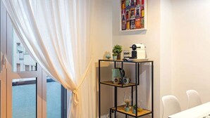 A modern room with a large window, a black metal shelf with decorative items, a white table, and a colorful artwork on the wall. - Easylife - Design and new flat in Navigli district (Milano)