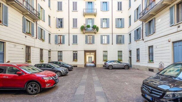 En innergård med parkerade bilar, en central entré och byggnader med balkonger.