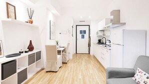A modern, well-lit kitchen with white cabinets and a built-in stove. A dining area with a table and chairs is visible, and a gray sofa is in the foreground. - Easylife - Bright and charming flat with balcony (Milano)