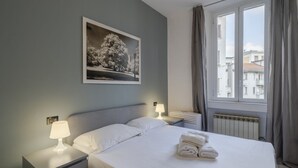 A hotel room with a bed, two bedside tables with lamps, a framed picture on the wall, and a window with curtains.