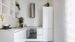 A compact kitchen with white cabinetry, a stainless steel range hood, and a built-in oven.